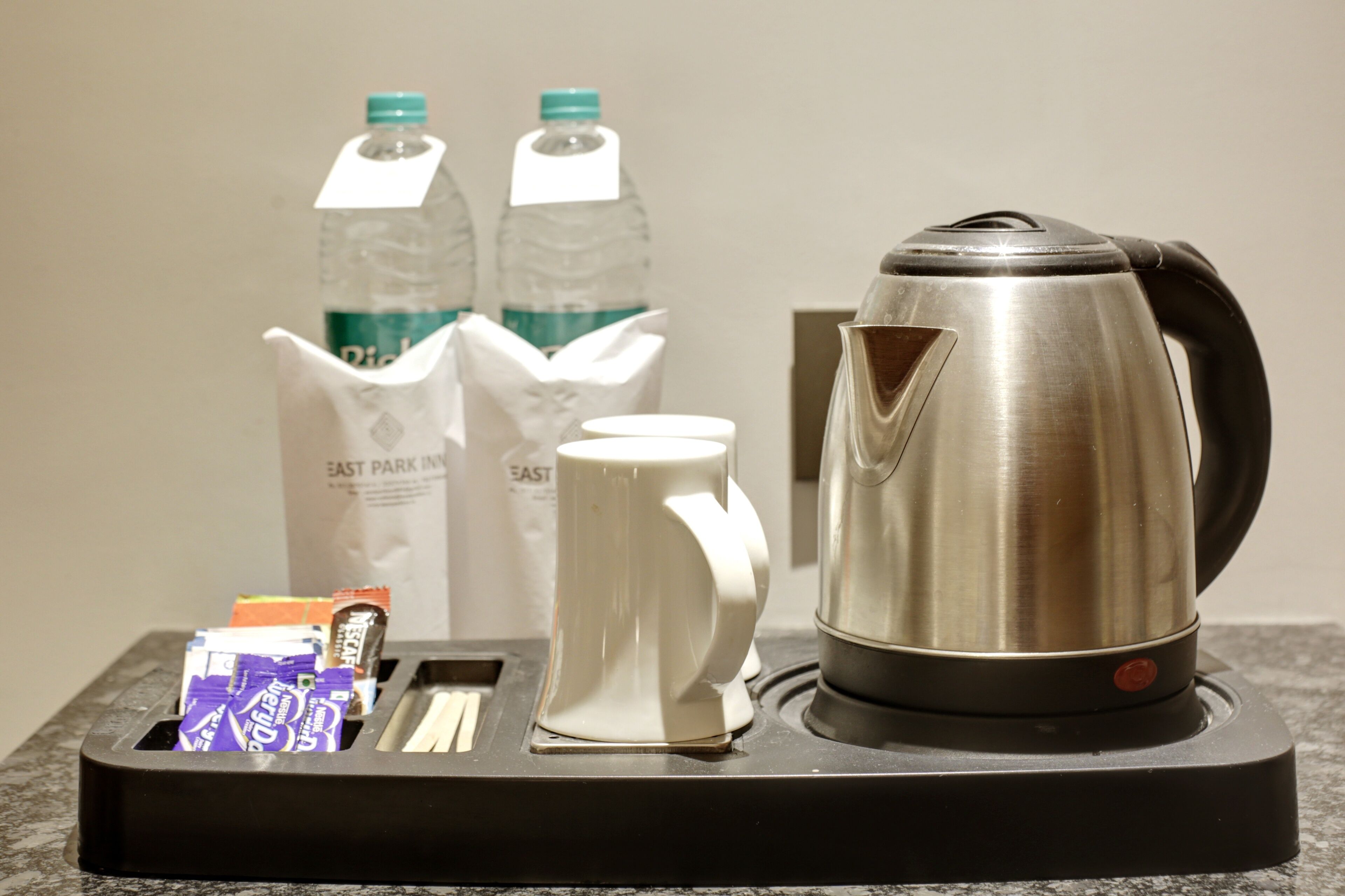 Eine Kaffeemaschine, eine Tasse, ein Tablett mit Milchkartons und eine Papiertasche auf einer Arbeitsplatte.