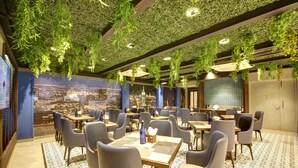 A restaurant with tables and chairs, a cityscape mural, hanging plants, and a patterned floor. - East Park Inn (New Delhi)
