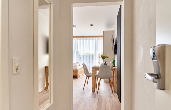 A modern interior with a dining area, wooden flooring, and a view through a doorway.