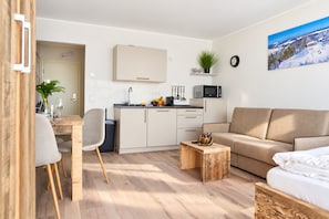 Ein modernes Wohnzimmer mit einer Couch, einem Esstisch mit Stühlen, einer Küchenzeile mit Schränken und einem kleinen Beistelltisch.