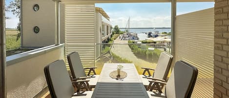 A covered outdoor seating area with a table and chairs, overlooking a marina with boats and a distant shoreline.
