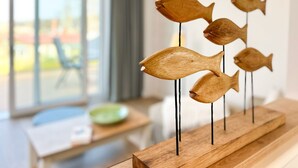 Une sculpture de poisson en bois est posée sur une table dans une pièce dotée d’une fenêtre et d’une chaise.