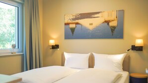 Une chambre d’hôtel avec un lit, deux lampes de chevet, une fenêtre avec des rideaux et un tableau au mur.