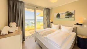 Une chambre d’hôtel avec un grand lit, une vue sur la mer par une porte coulissante et un tableau au mur.