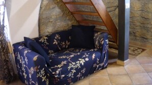 A corner room with a stone wall, a wooden ladder, a blue floral sofa, and a tiled floor. - Parva Domus in 29 (Morlupo)