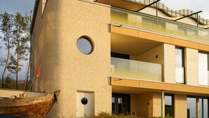 A modern building with a curved brick facade, a round window, and a balcony. - Bright Top-Floor Suite with Large Rooftop Terrace and Harbor View (Rankwitz)