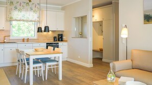 A modern kitchen with white cabinets, a dining table with chairs, and a coffee machine. There is a sofa and a floor lamp in the living area. - Spacious Top-Floor Suite with Large Rooftop Terrace – Ideal for Families (Rankwitz)