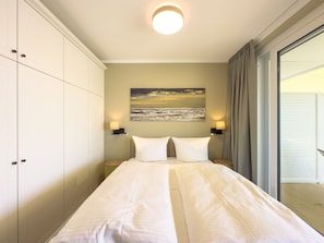 Une chambre à coucher avec un lit, deux lampes de chevet, un tableau et une vue sur l’extérieur.