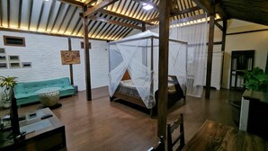 Una habitación amplia con techo alto, una cama con dosel, un sofá, una mesita de café y un televisor.
