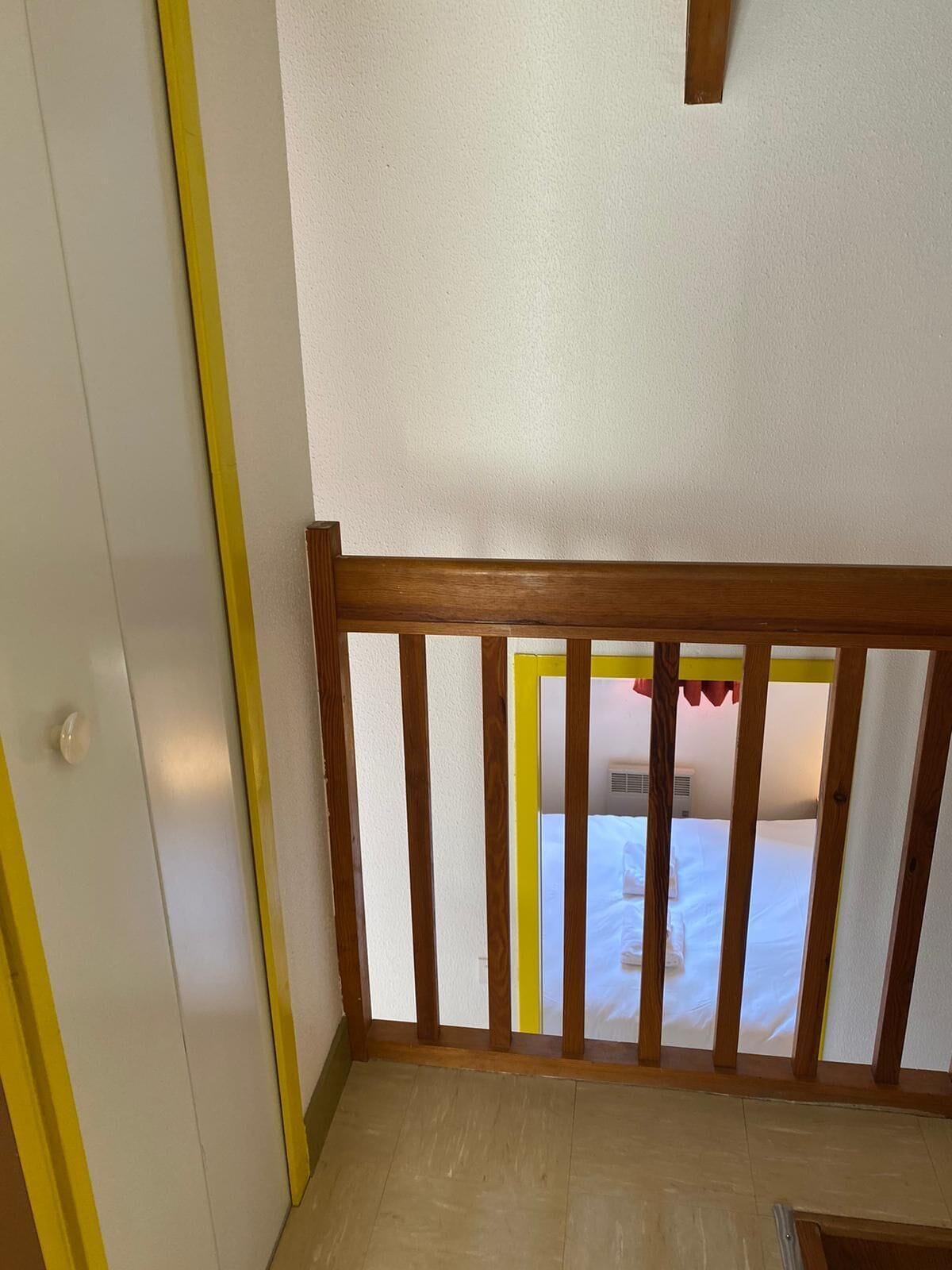 Une pièce avec une balustrade en bois, une porte blanche et une vue sur un lit recouvert de draps blancs.