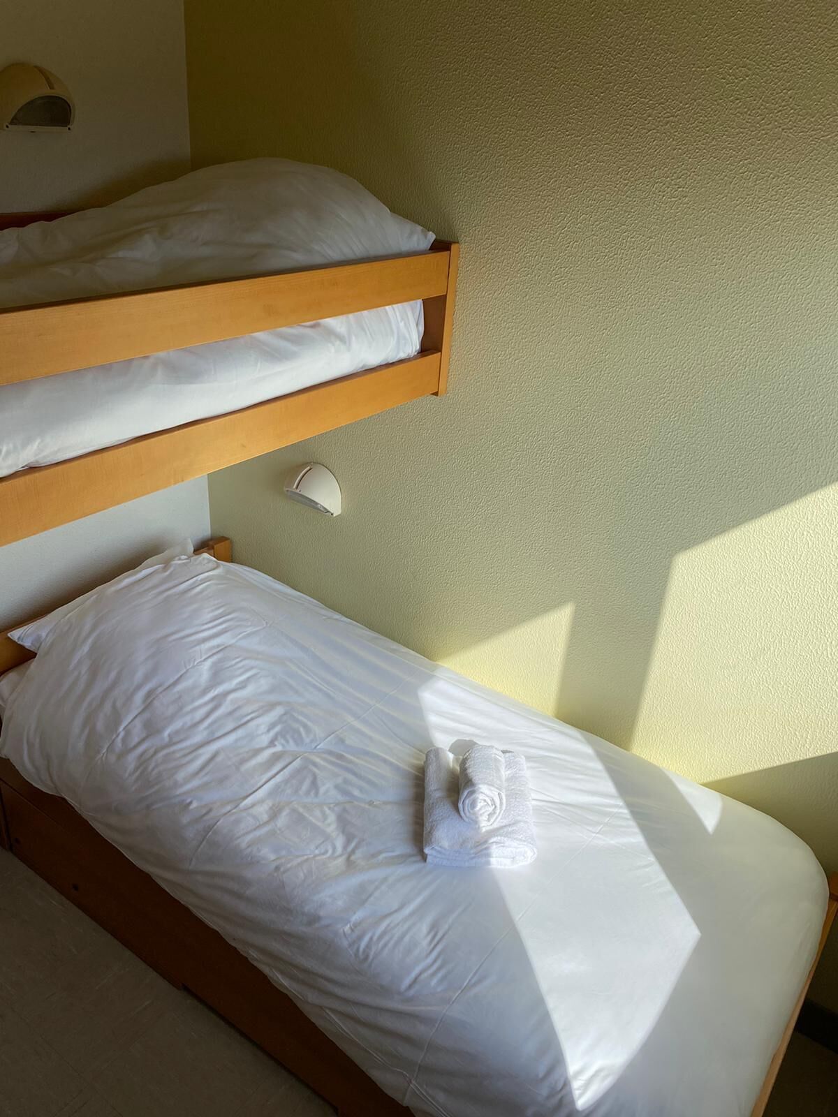 A bunk bed with white bedding and a rolled towel on the lower bunk.