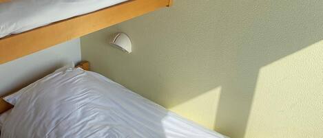 A bunk bed with white bedding and a rolled towel on the lower bunk.