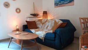 A cozy living room with a blue sofa, a small round table, and a ship model on a shelf. - Luxury Lakeside T3: Modern, Bright, Near Beach, WiFi, Parking (Soorts-Hossegor)
