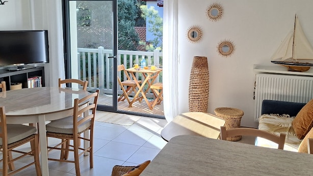 A modern living room with a dining area, a TV, and a balcony with a view of greenery. - Luxury Lakeside T3: Modern, Bright, Near Beach, WiFi, Parking (Soorts-Hossegor)