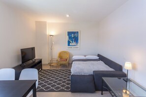 A modern hotel room with a bed, a TV, a chair, a desk, and a lamp.