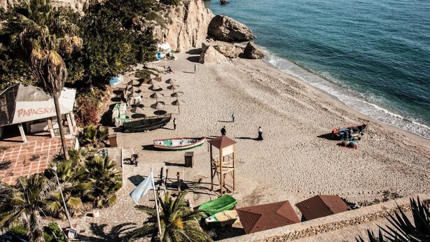 Una playa con sombrillas, una torre de salvavidas y un pequeño bote.