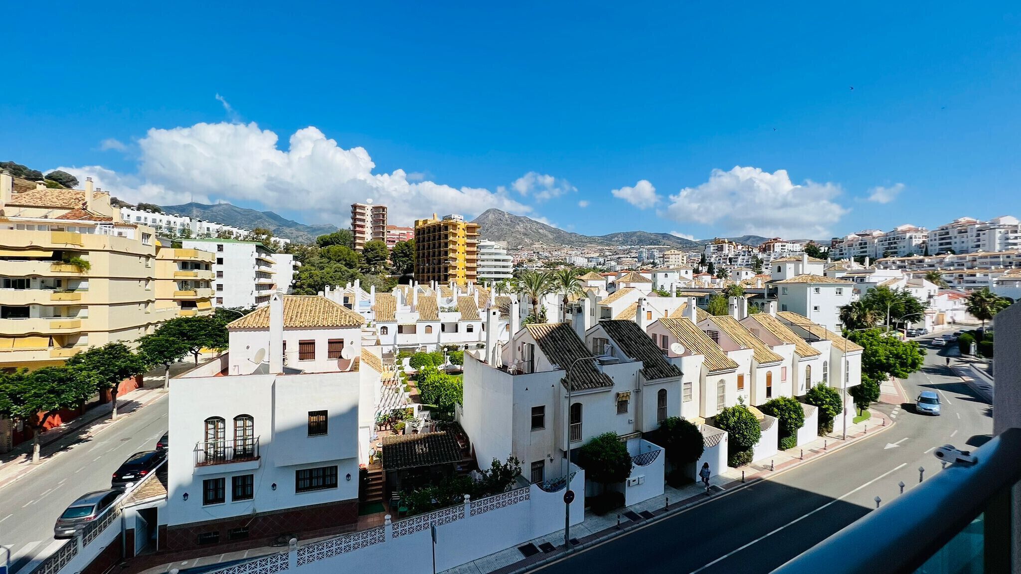 A coastal cityscape with white buildings, a clear blue sky, and a mountain in the background.