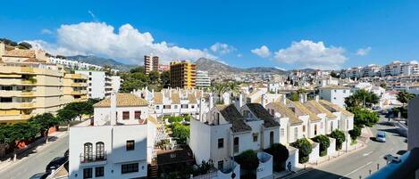 A coastal cityscape with white buildings, a clear blue sky, and a mountain in the background.