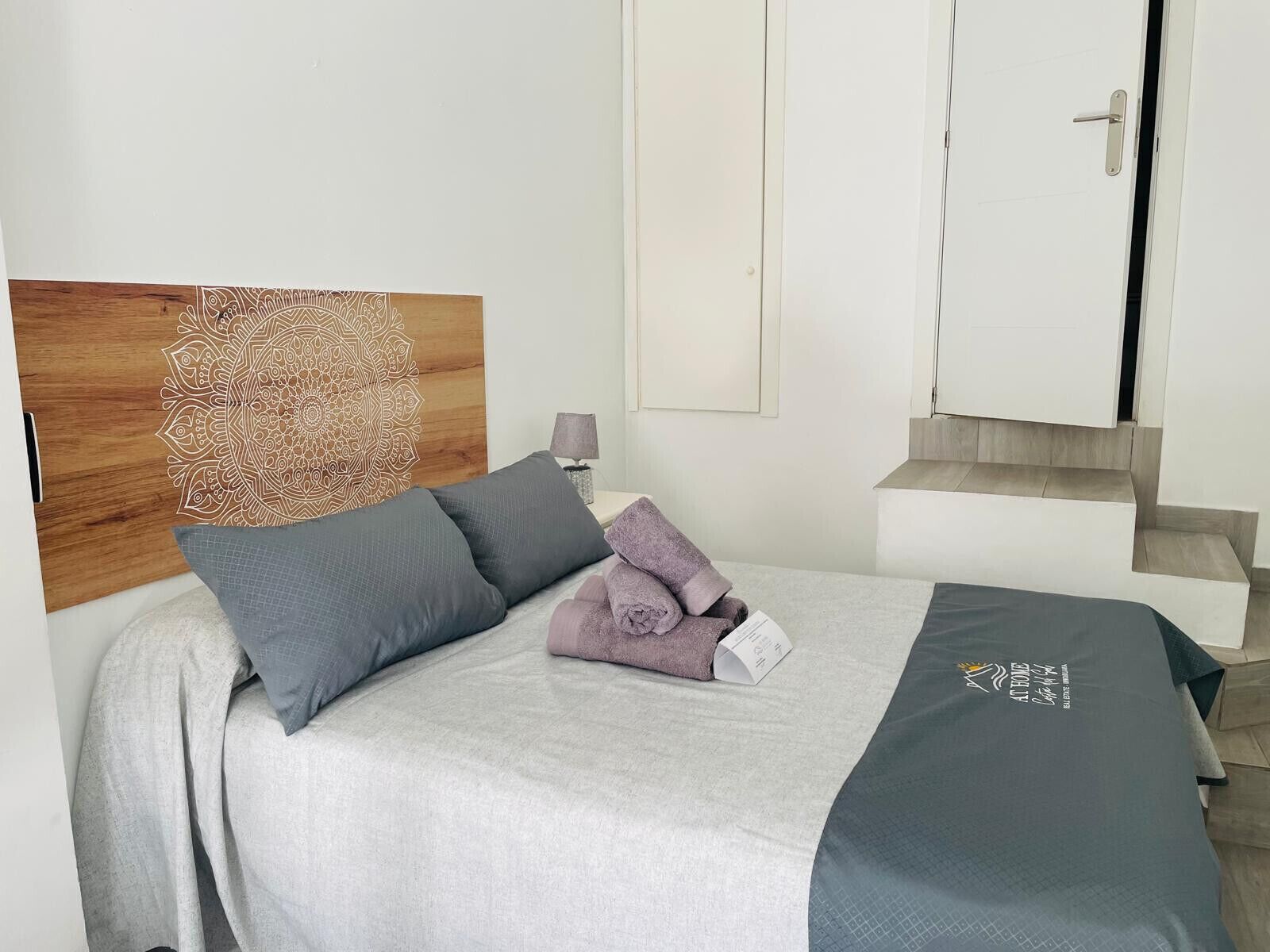 A neatly made bed with a grey and blue bedspread, two pillows, and a folded towel.