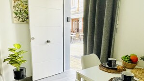 Un coin repas avec une table blanche, des chaises, un panier de fruits et une plante en pot.