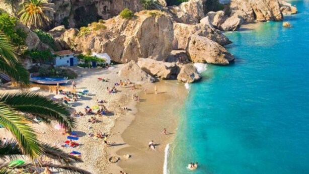 Une ville côtière dotée d’une plage, de falaises rocheuses et de montagnes en arrière-plan.