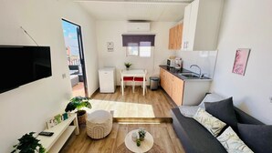 Un espace de vie compact comprenant un coin cuisine, un coin repas et un coin salon avec un canapé et un pouf.
