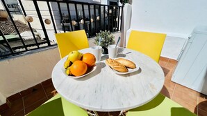 Une table ronde surmontée d’un plateau en marbre blanc, entourée de chaises jaunes. Sur la table, on trouve des assiettes remplies de fruits et de pain.