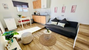 Un espace de vie compact comprenant un coin cuisine, un canapé avec des coussins, une table à manger avec des chaises et une petite table basse ronde.