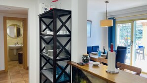 Una cocina moderna con una estantería negra, un comedor con sillas azules y vistas al exterior.