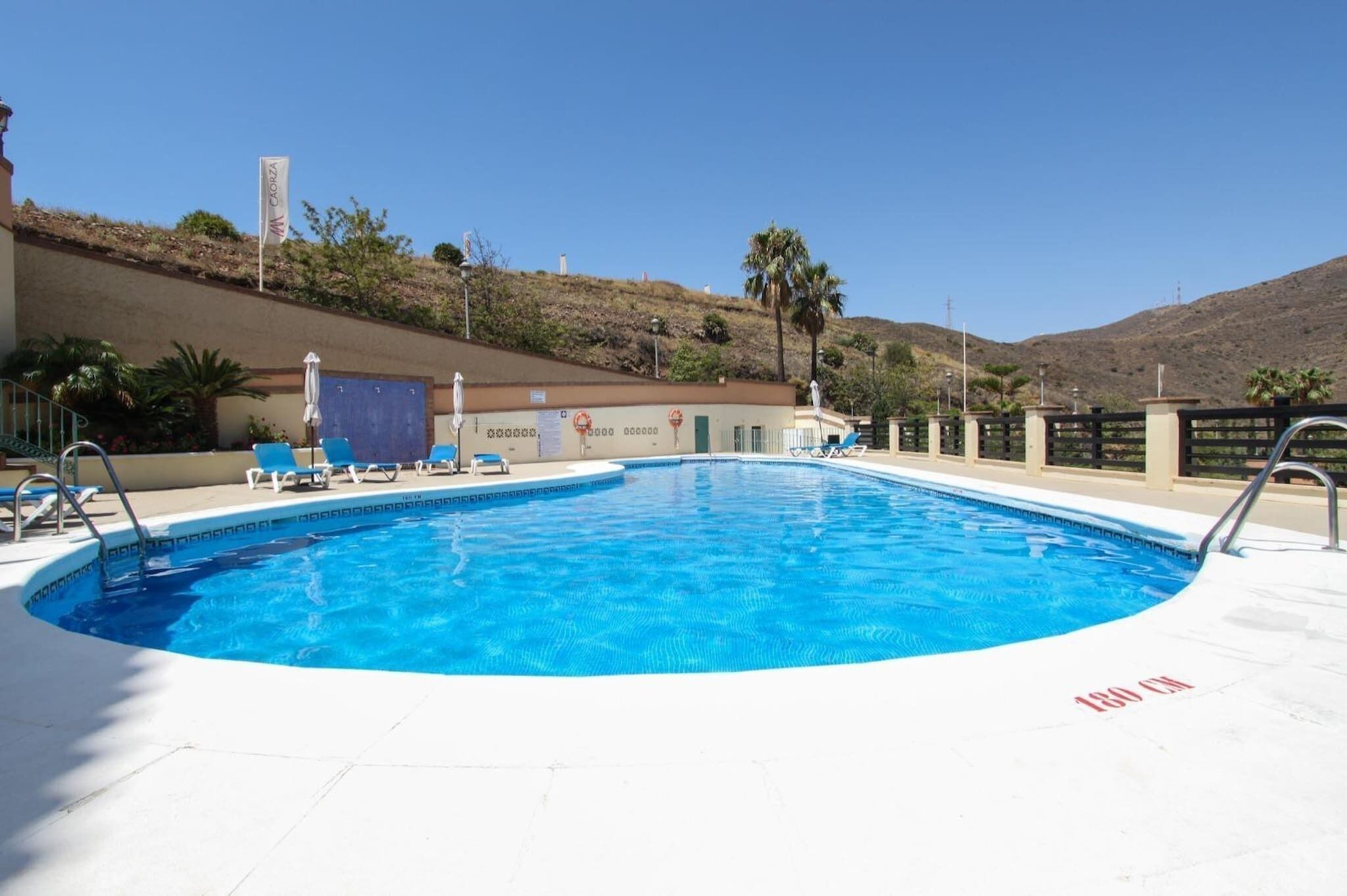 Una piscina con sillas de descanso, una bandera y una colina al fondo.