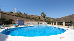 Una piscina con sillas de descanso, una bandera y una colina al fondo.