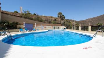 Una piscina con sillas de descanso, una bandera y una colina al fondo.