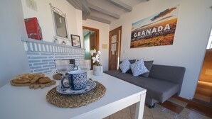 Een gezellige zithoek met een witte tafel gedekt voor het ontbijt, een grijze bank en een muur met een 'Granada' poster.