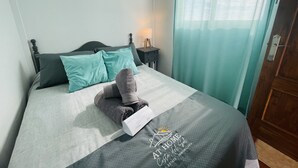 Een net opgemaakt bed met een grijze en teal deken, een paar opgevouwen grijze handdoeken, en een wit kussen met een logo.