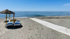 A beach with a thatched-roof structure, two lounge chairs, and a wooden walkway. - Apartment Urb Laguna Beach Torrox Costa (Torrox Costa)