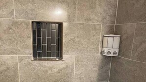 A bathroom with a bathtub, tiled walls, a window with bars, and a wall-mounted heater.