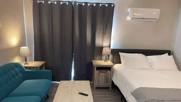 Habitació d'hotel amb un llit, un sofà, una taula petita, dues mesetes de nit amb làmpades i un aire condicionat.