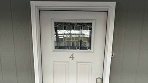 Una porta blanca amb el número 4, una petita finestra amb reixes i un felpú amb la paraula 'hello'.