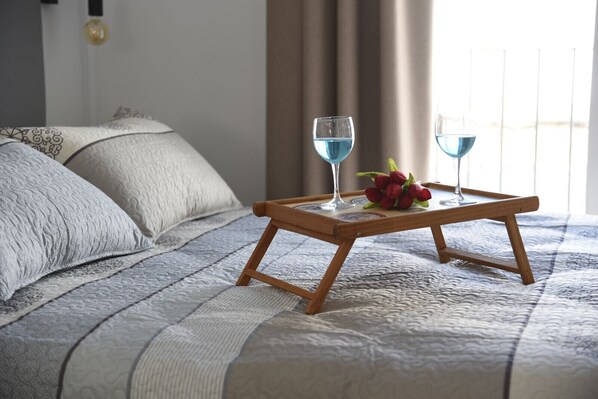 A bed with a quilted cover, two bedside tables with glasses of blue liquid, and a tray with red flowers.