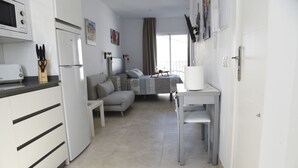A modern kitchen with a refrigerator, microwave, and toaster. There is a dining area with a table and chairs. The room has a large window with curtains. - Platero penthouse in the center of nerja (Nerja)