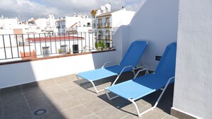 A rooftop terrace with two blue lounge chairs, a metal railing, and a view of surrounding buildings. - Platero penthouse in the center of nerja (Nerja)