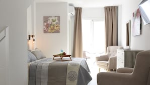 A bedroom with a bed, a bedside table with a glass of water and flowers, a chair, a desk, and a window with curtains. - Platero studio in the center of nerja (Nerja)