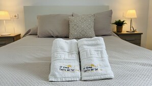 Una cama bien hecha con dos toallas, un almohadón y dos mesitas de noche con lámparas.