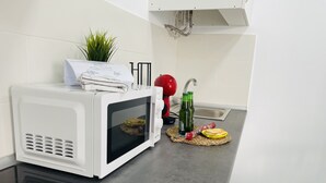 Una cocina con un microondas blanco, un hervidor rojo y una planta pequeña en la encimera.