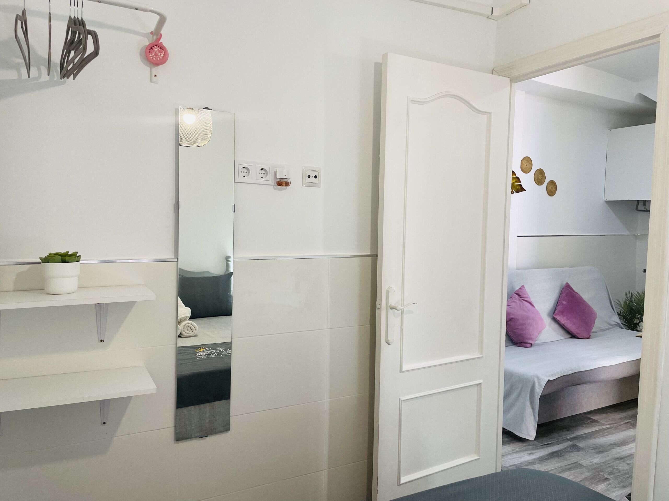 A modern bedroom with a white door, a bed with a grey and white bedspread, and a small bedside table with a plant.