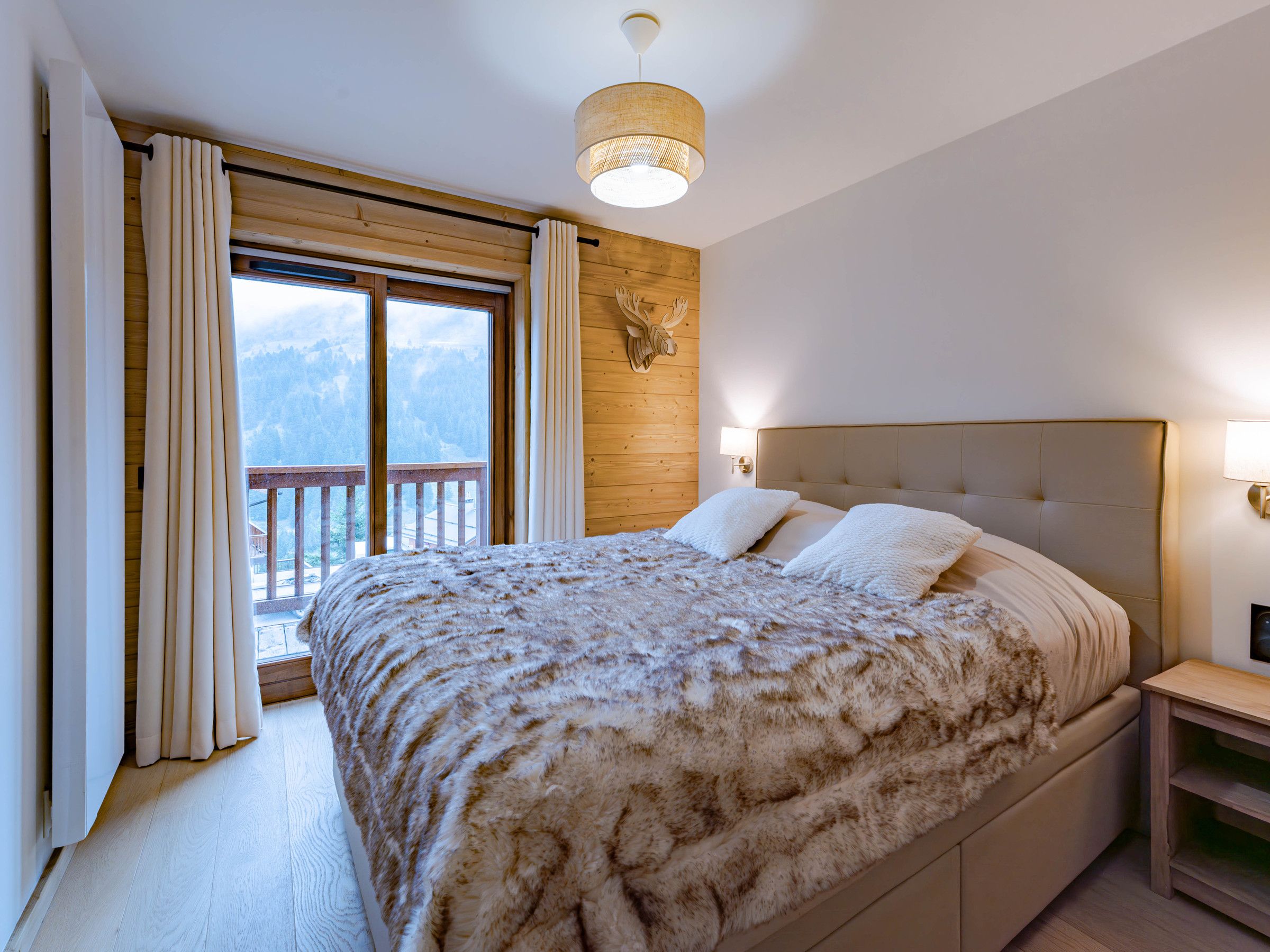 A bedroom with a large bed, wooden walls, a view of mountains, and a balcony.