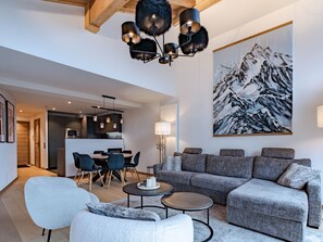 A modern living room with a grey sofa, a white armchair, and a dining area with a wooden table and chairs.