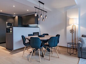 A modern kitchen with built-in appliances, a dining area with a wooden table and blue chairs, and a floor lamp.