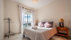 Ein Schlafzimmer mit einem Bett, zwei Nachttischen, einer Lampe, einem Kleiderständer und einem Fenster mit Vorhängen.