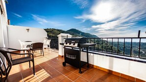 Ein Balkon mit Grill, Stühlen und Blick auf eine Berglandschaft.